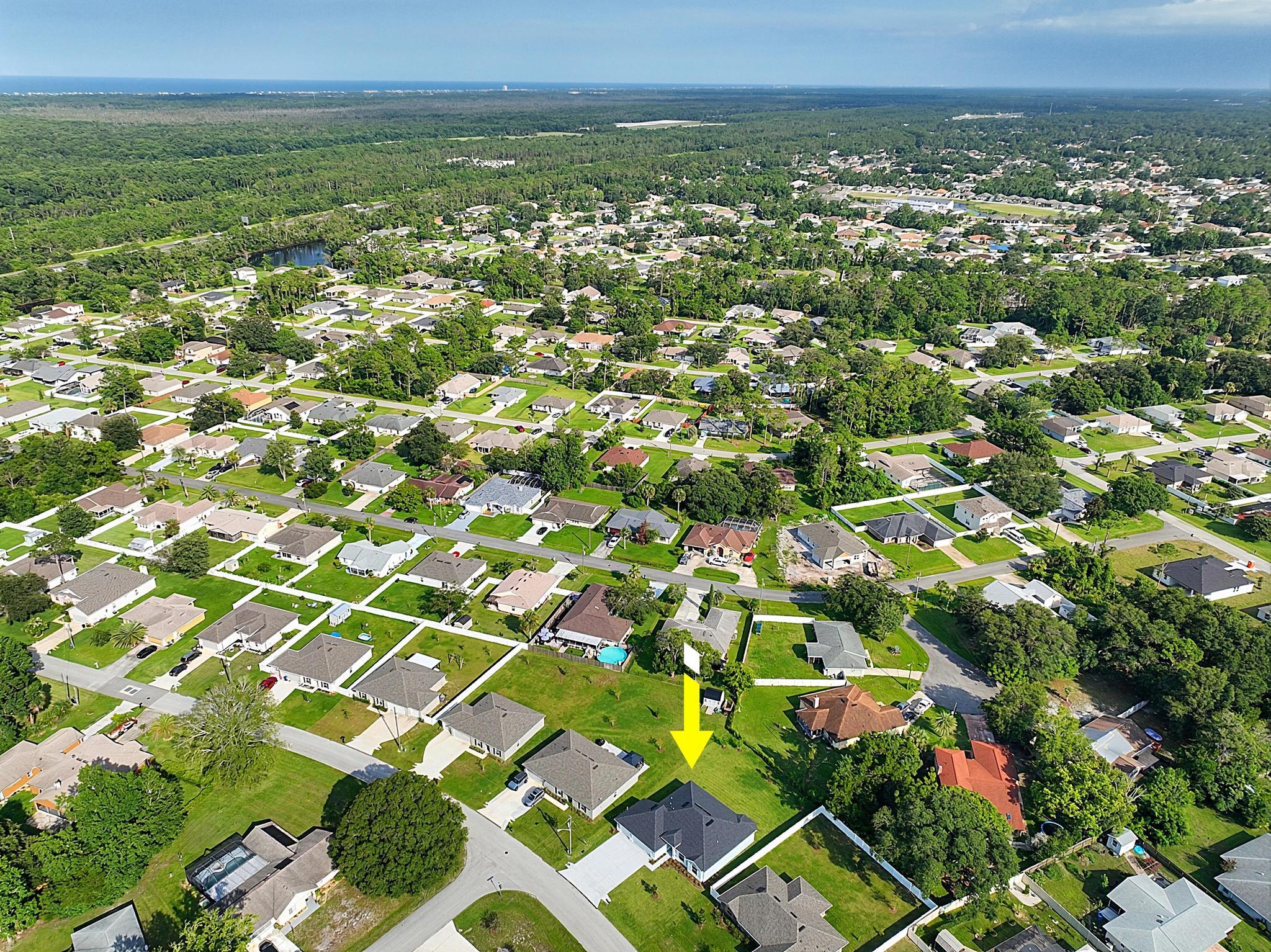 Wider aerial view of the community with a yellow arrow marking the home